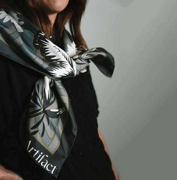 Person wearing a patterned scarf with 'Artifact' branding on a plain background