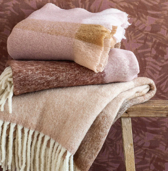 Stack of patterned blankets on a wooden surface with a textured purple background