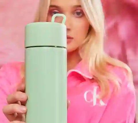 Person holding a light green drink Bottle with a pink background