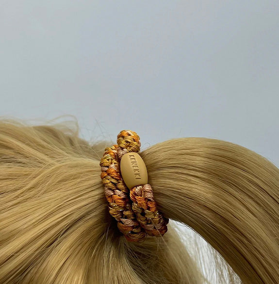 Hair tie with a brand label on blonde hair against a light gray background