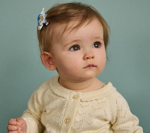 Baby wearing a cream-colored knitted cardigan against a light blue background