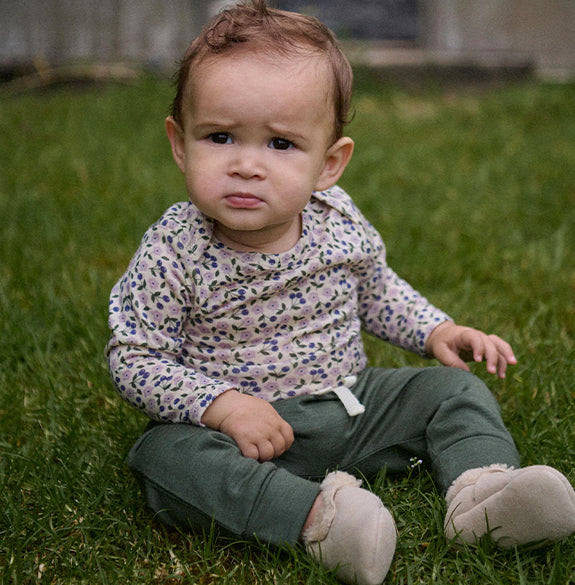 Child sitting on grass wearing a patterned shirt and green pants