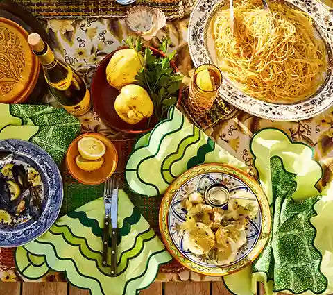 Dining table set with Italian pasta dishes and wine bottles on a patterned tablecloth.
