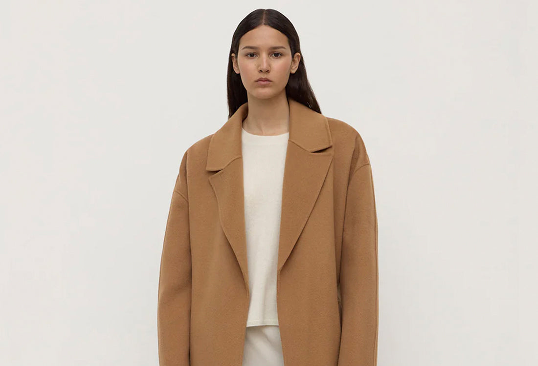 Woman wearing a brown coat over a white shirt on a plain background