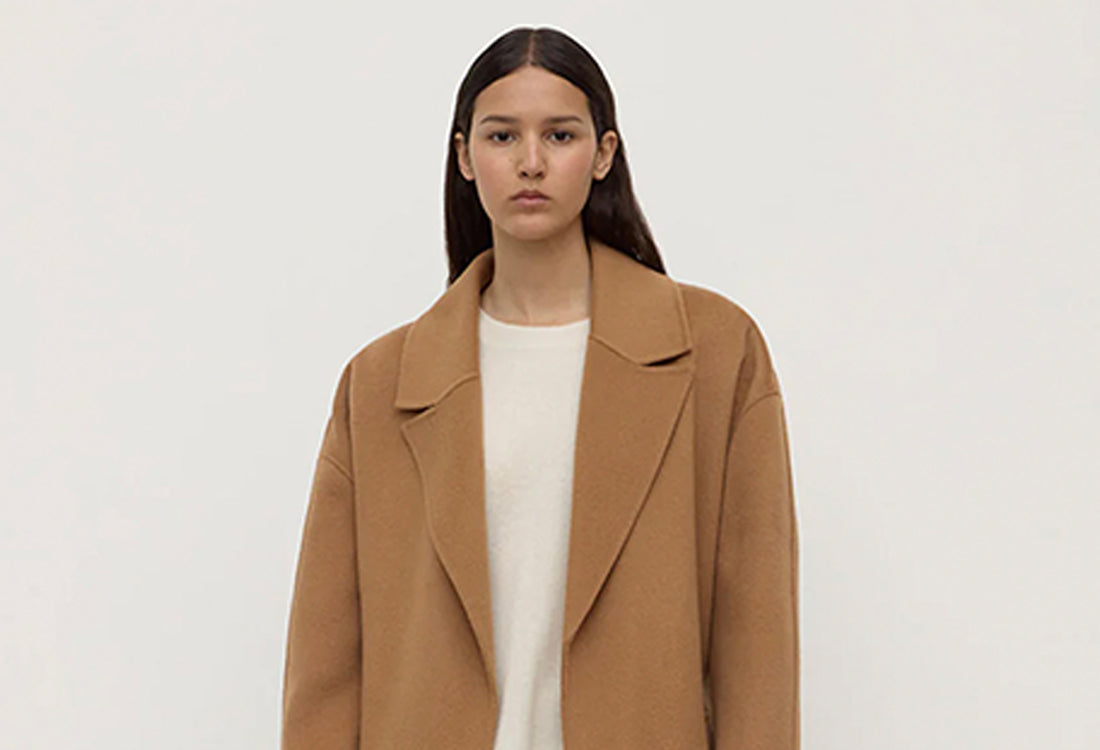 Woman wearing a brown coat over a white shirt on a plain background