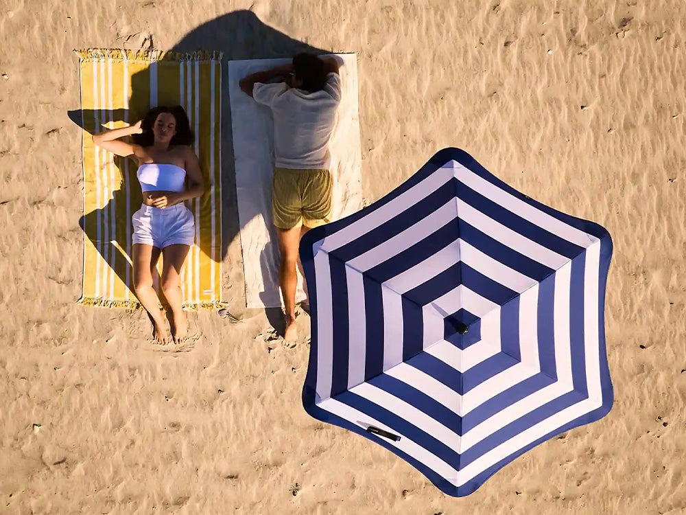 Two people on towels with a striped beach umbrella in the sand