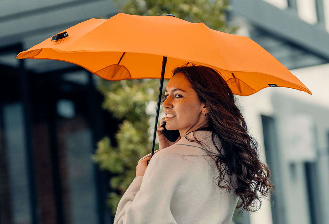 Woman holding an orange umbrella outdoors with a blurred background