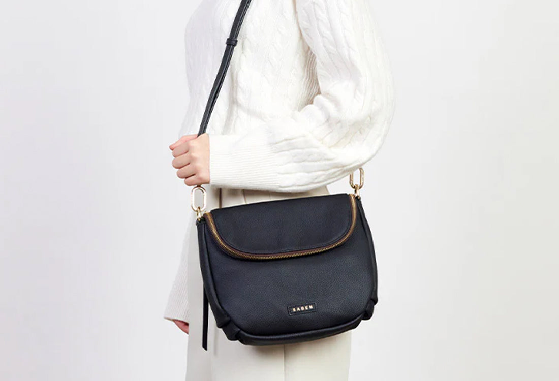 Person holding a black crossbody bag with a white background