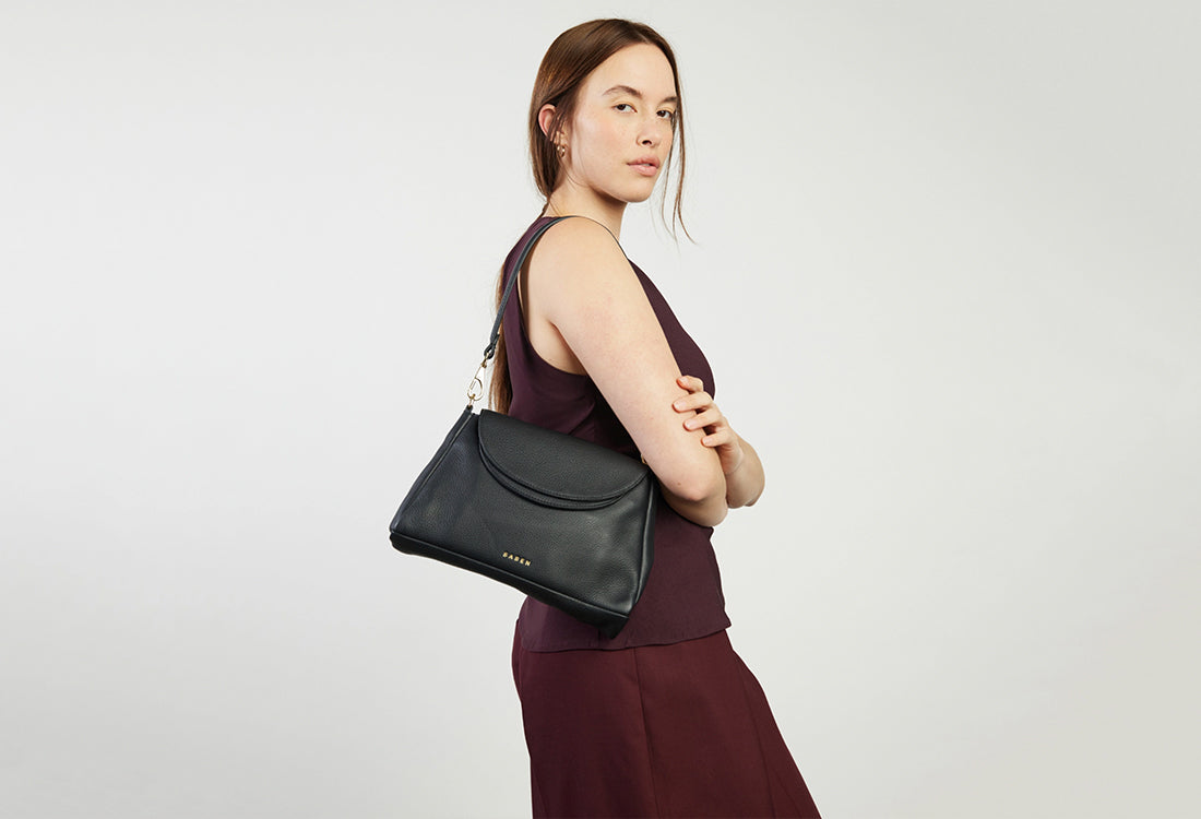 Woman holding a black handbag against a plain background