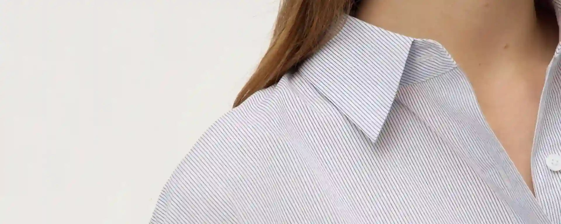 Close-up of a person wearing a light blue striped shirt with a plain background