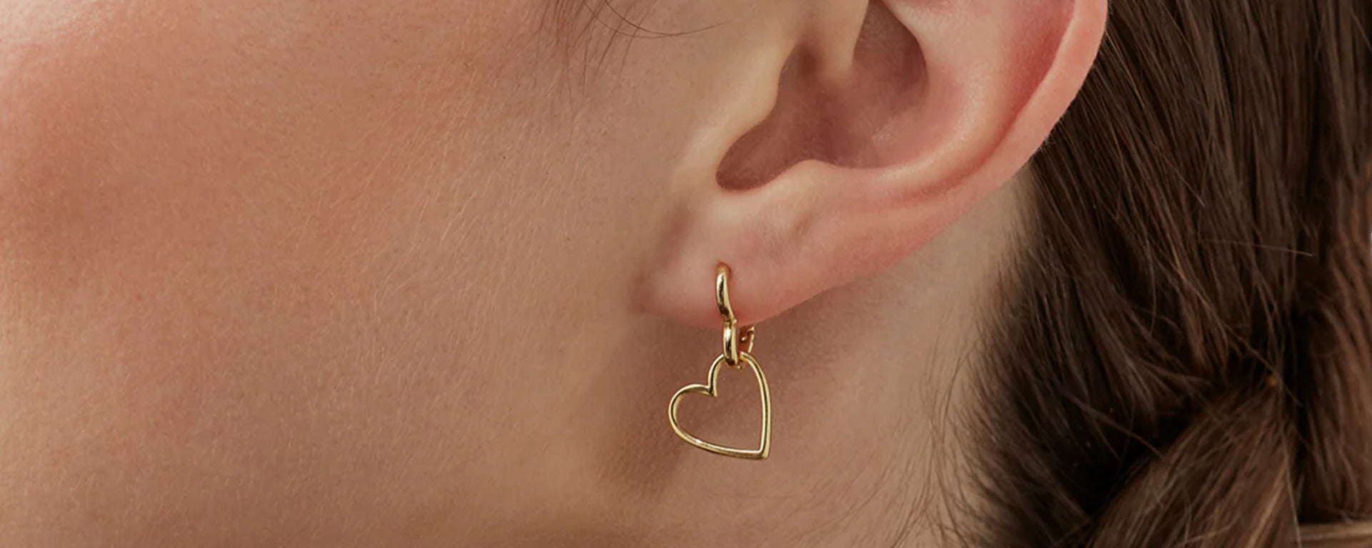 Gold heart-shaped earring worn by a person with brown hair.