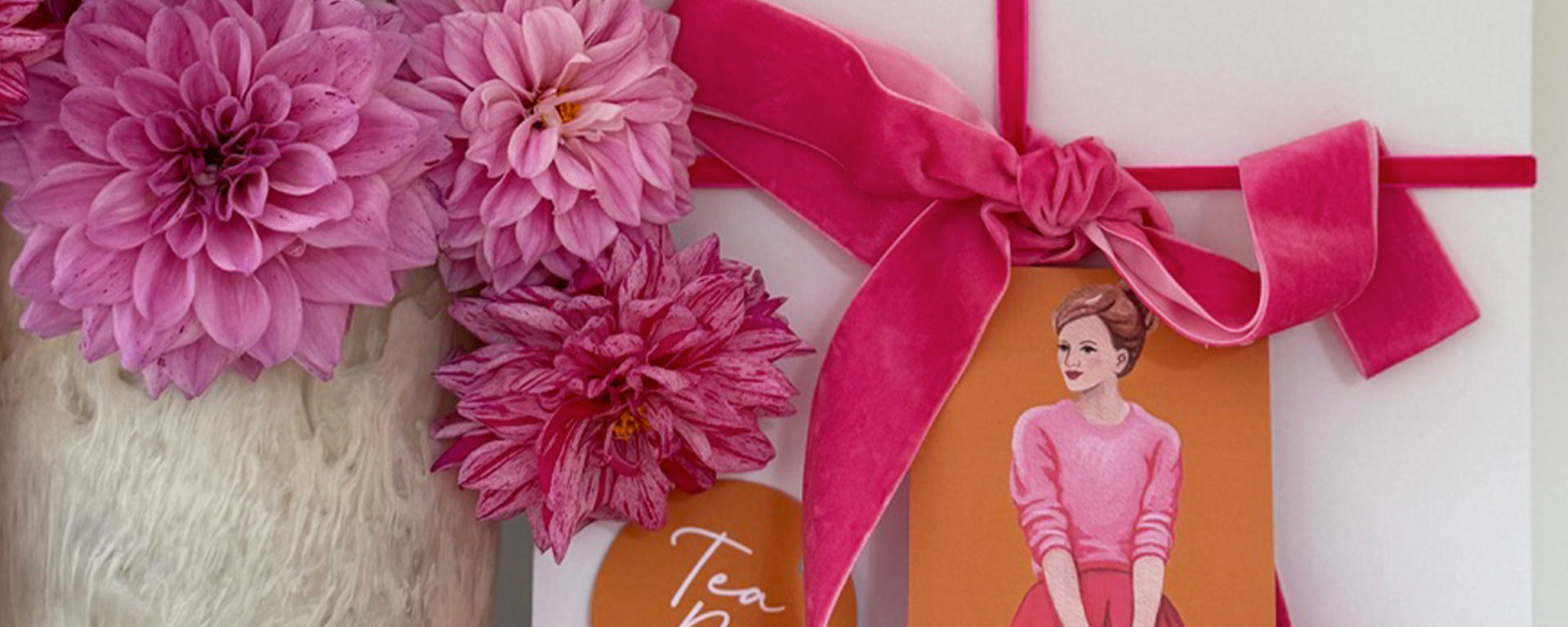 Gift box with pink flowers and a card featuring an illustration of a person in a pink sweater.