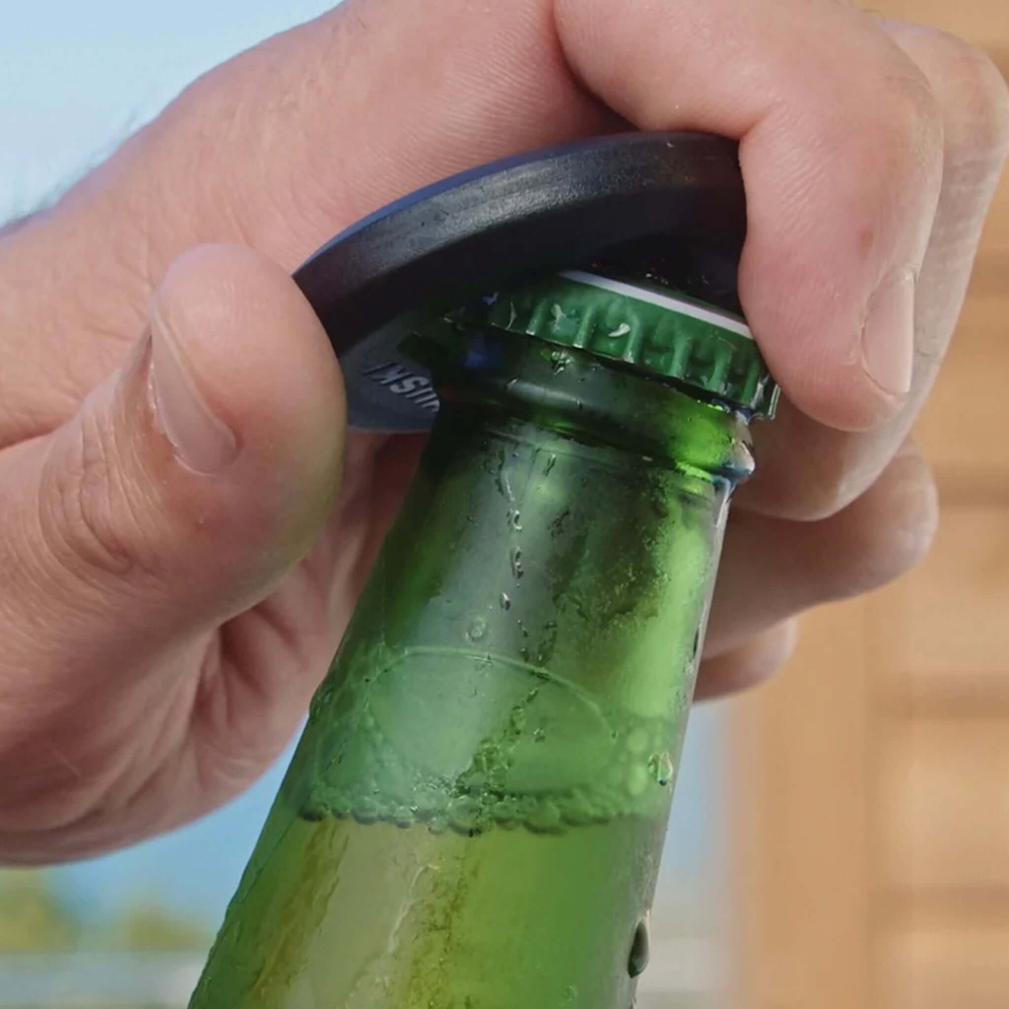 Huski 3-in-1 Bottle Opener Keyring in action popping a crown cap off a beer bottle.