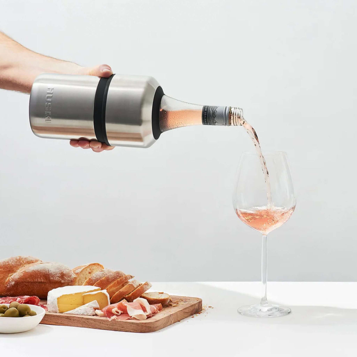 Huski Wine Cooler - White pouring rose wine into a glass with a charcuterie board in the background.