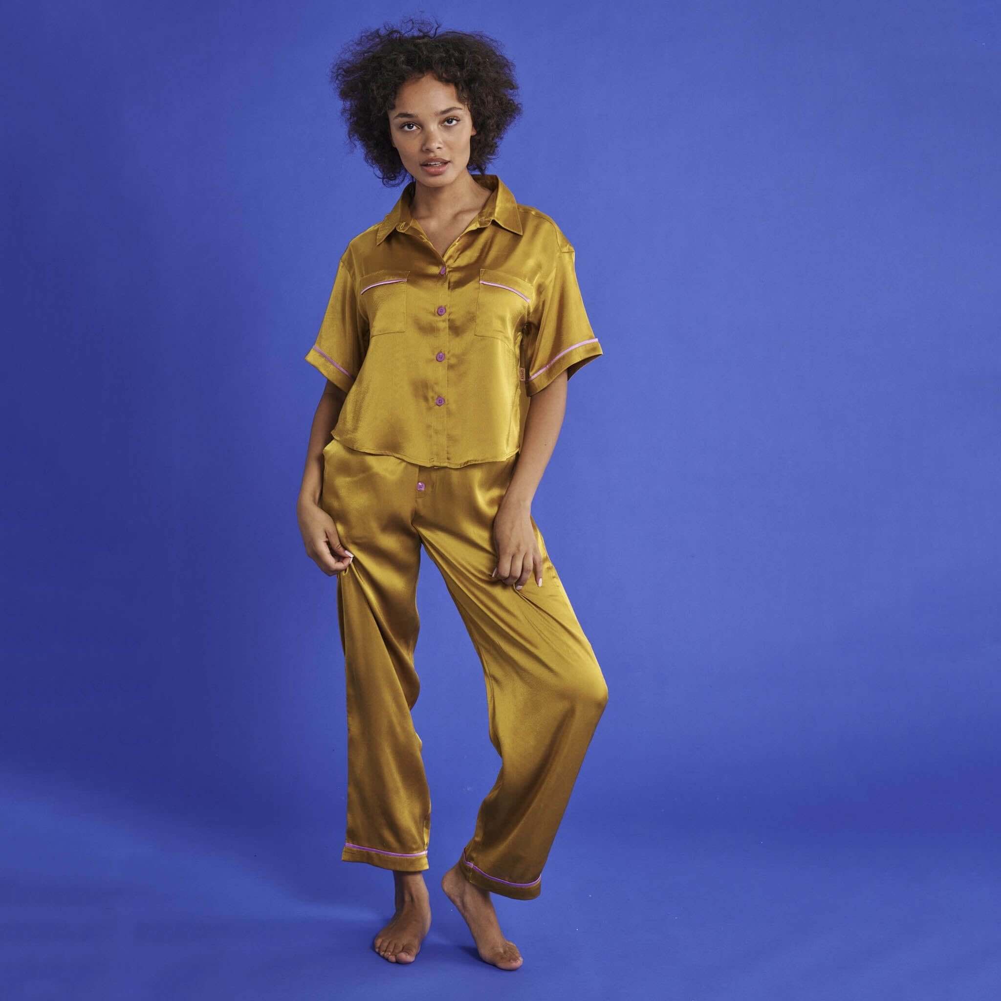 Alt Tag: Kip & Co Satin Short Sleeve Shirt & Pants Pyjama Set - VaVaVoom gold satin pyjamas with violet buttons, model front view