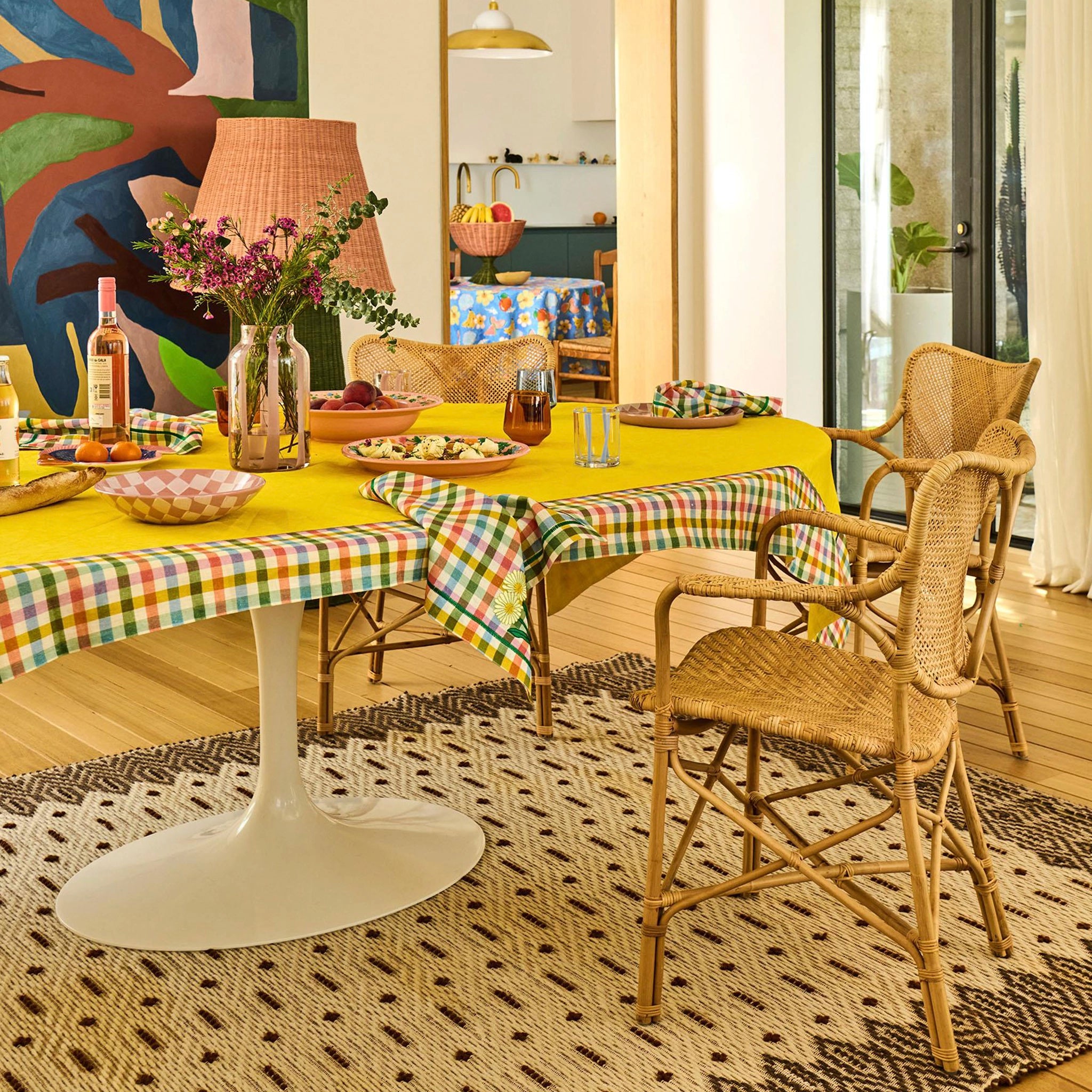 Dining room with a yellow tablecloth, plaid tablecloth, and wicker chairs.