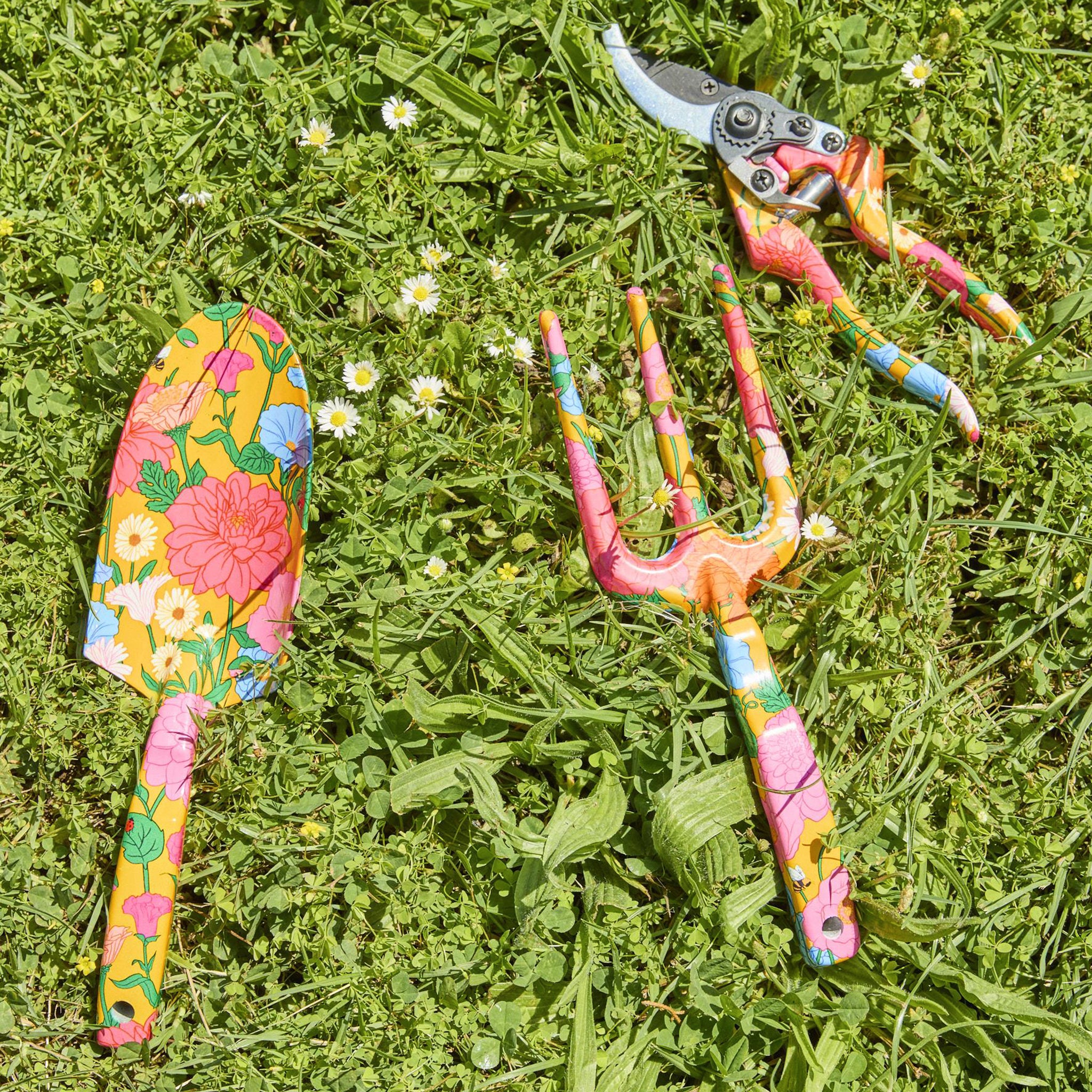 Colorful garden tools including a trowel and pruners on grass with flowers.