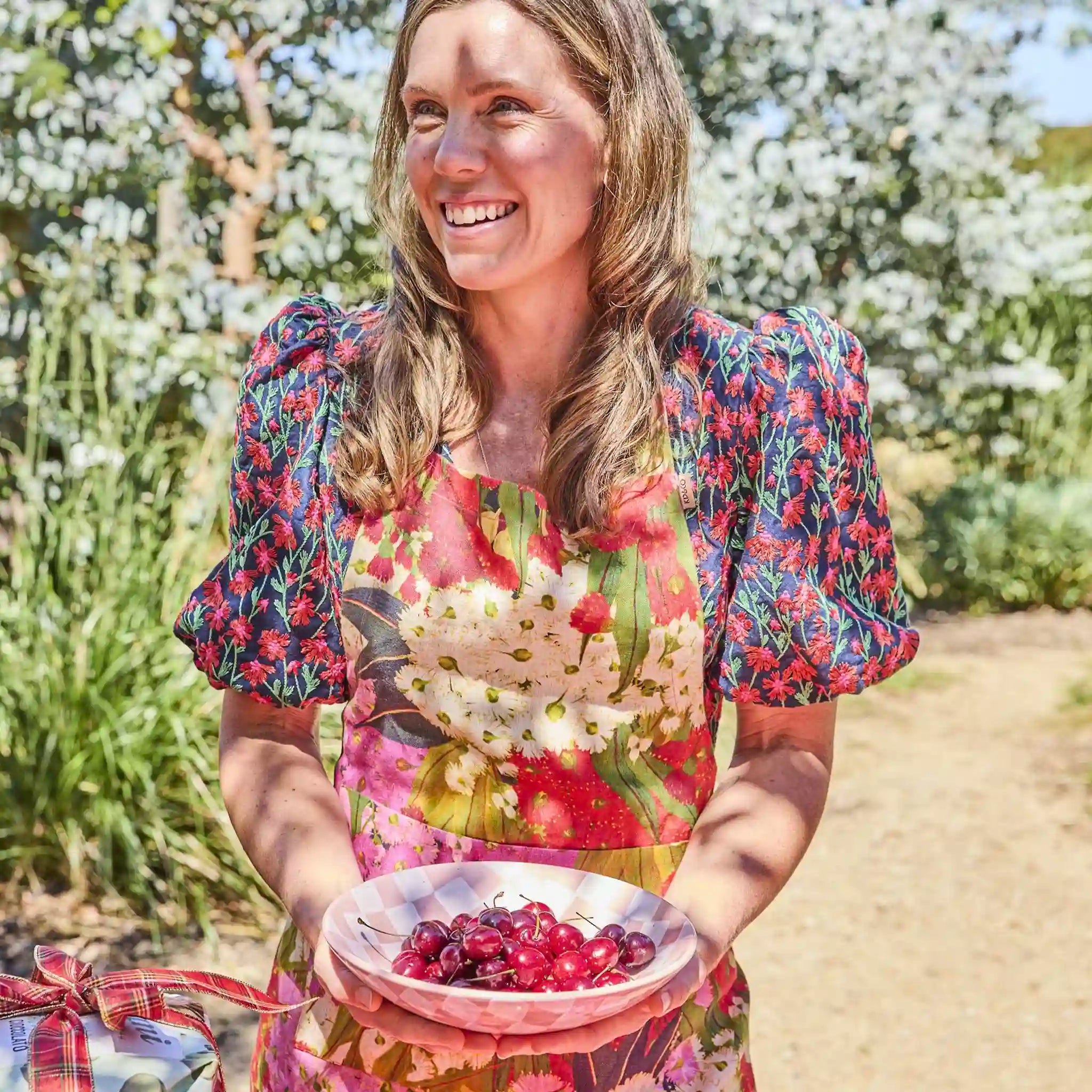 Woman holding a bowl of cherries in a garden setting