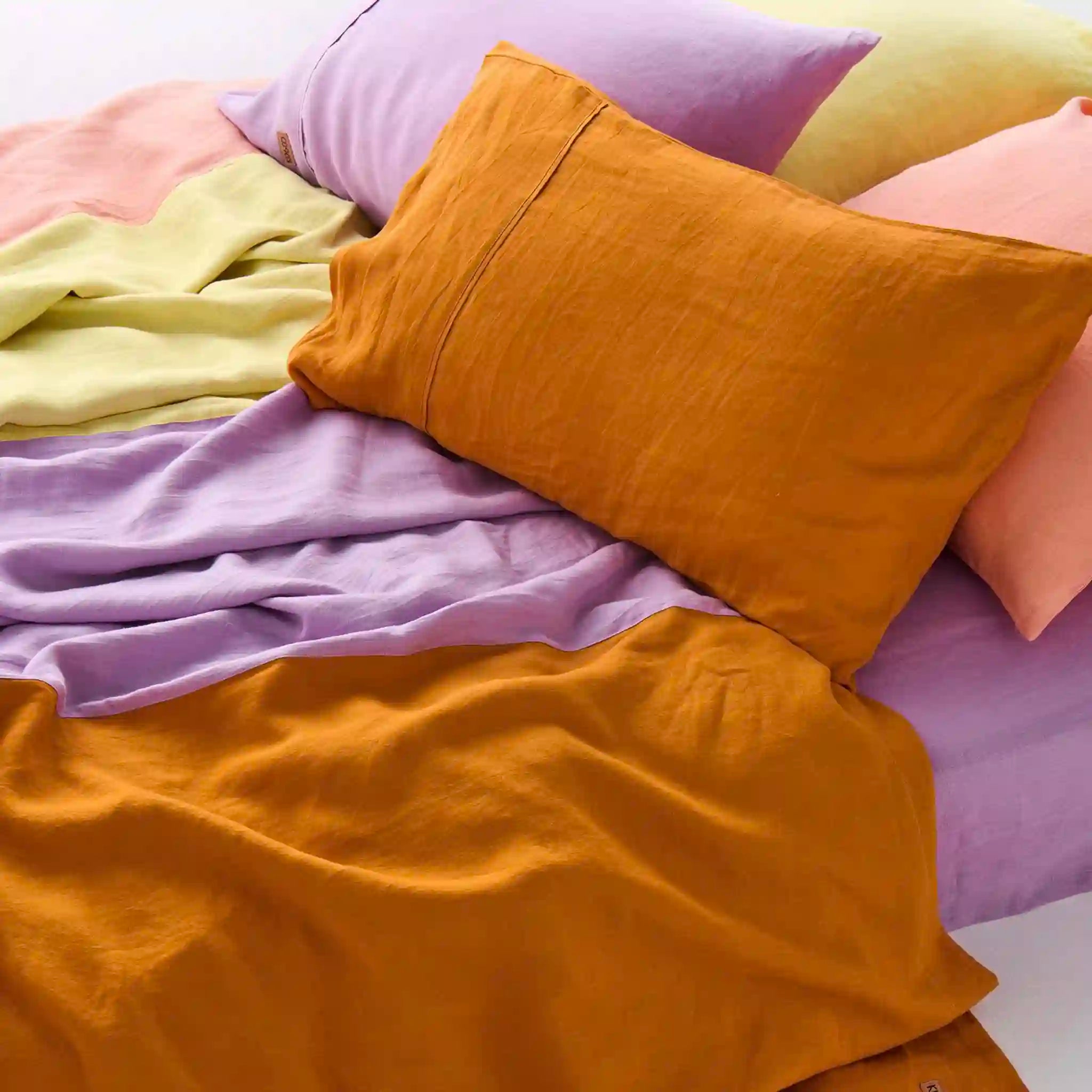 Colorful bedding with mustard yellow, pink, and purple pillows and blankets.