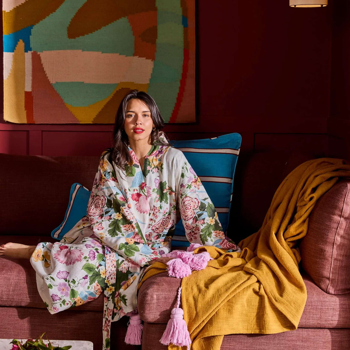 Kip & Co Linen Robe - Belle Floral model relaxing on a couch adorned with colorful pillows.