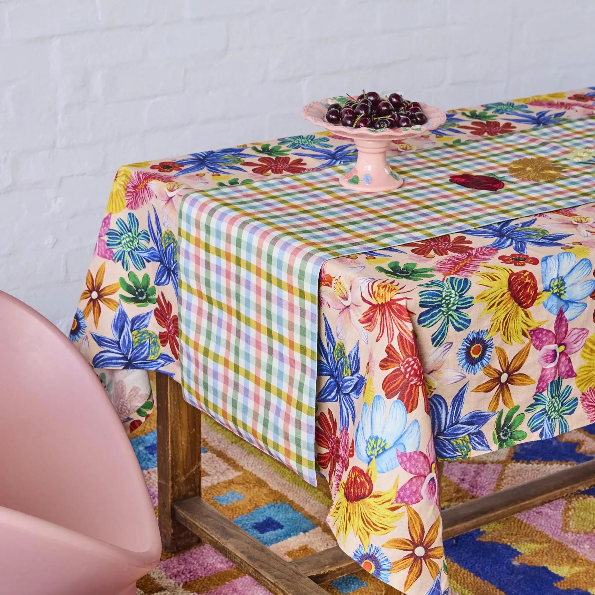 Colorful floral and checkered tablecloth on a wooden table with a white wall background.