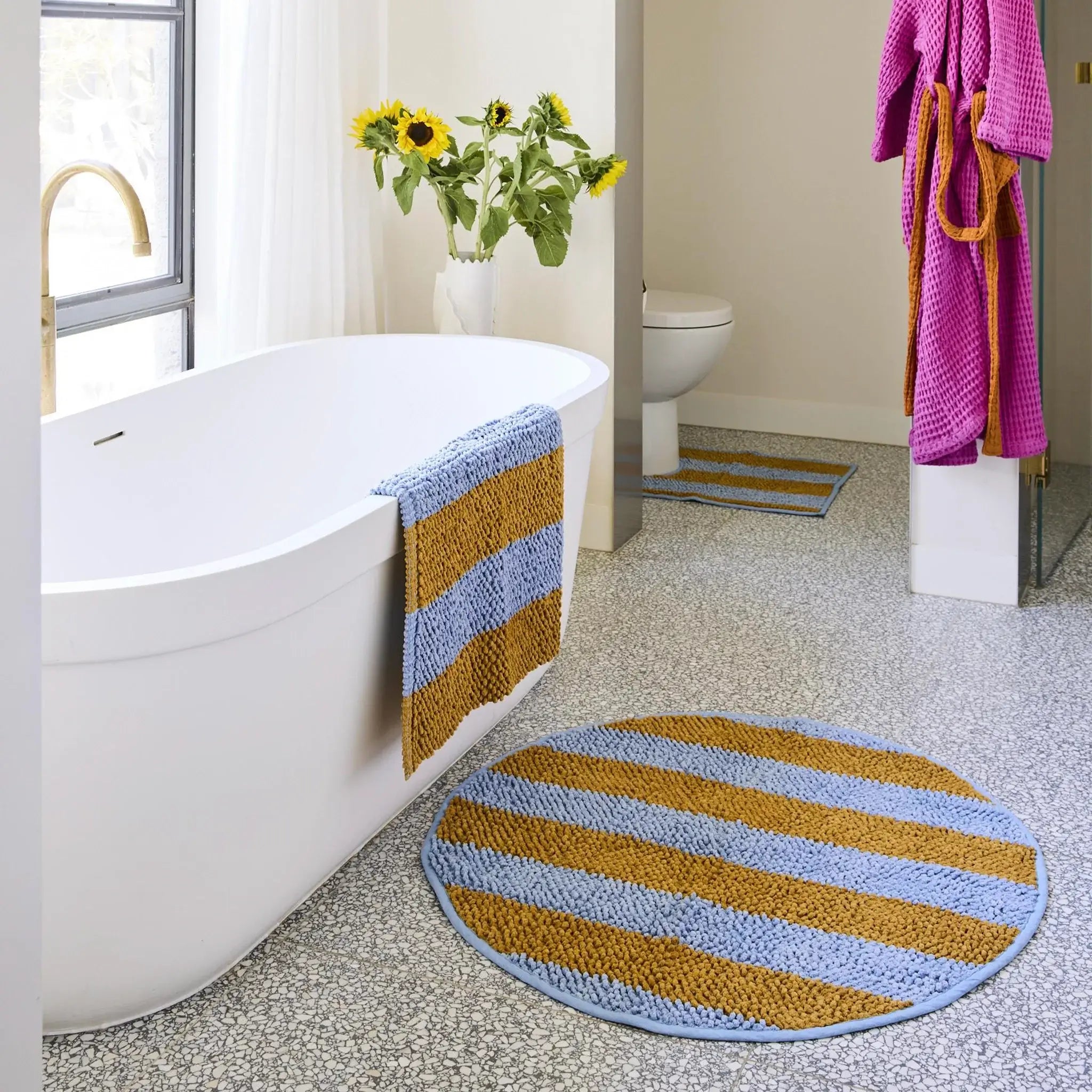Bathroom with a striped bath mat, towel, and flowers.