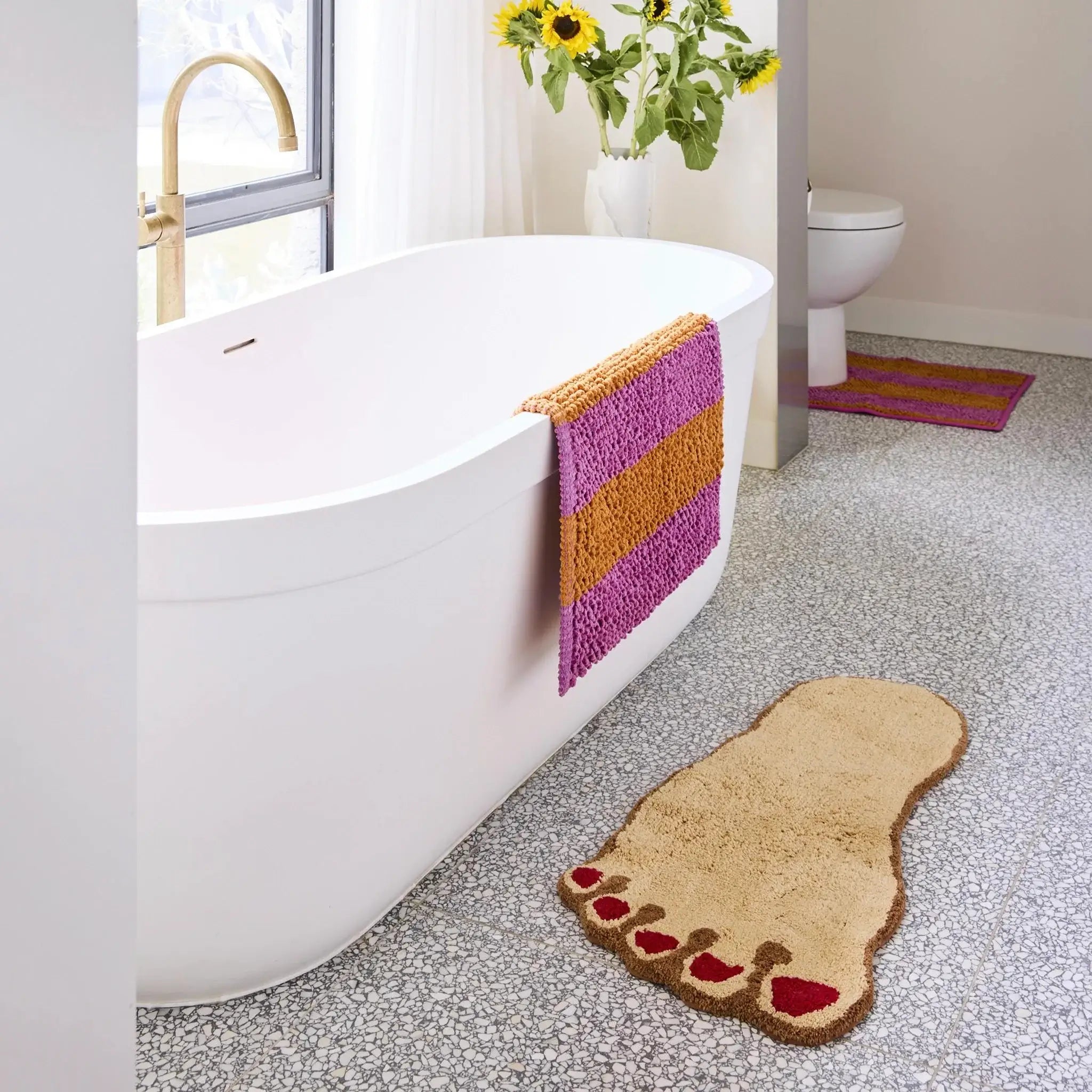 Bathroom with a bathtub, foot-shaped rug, and decorative elements.