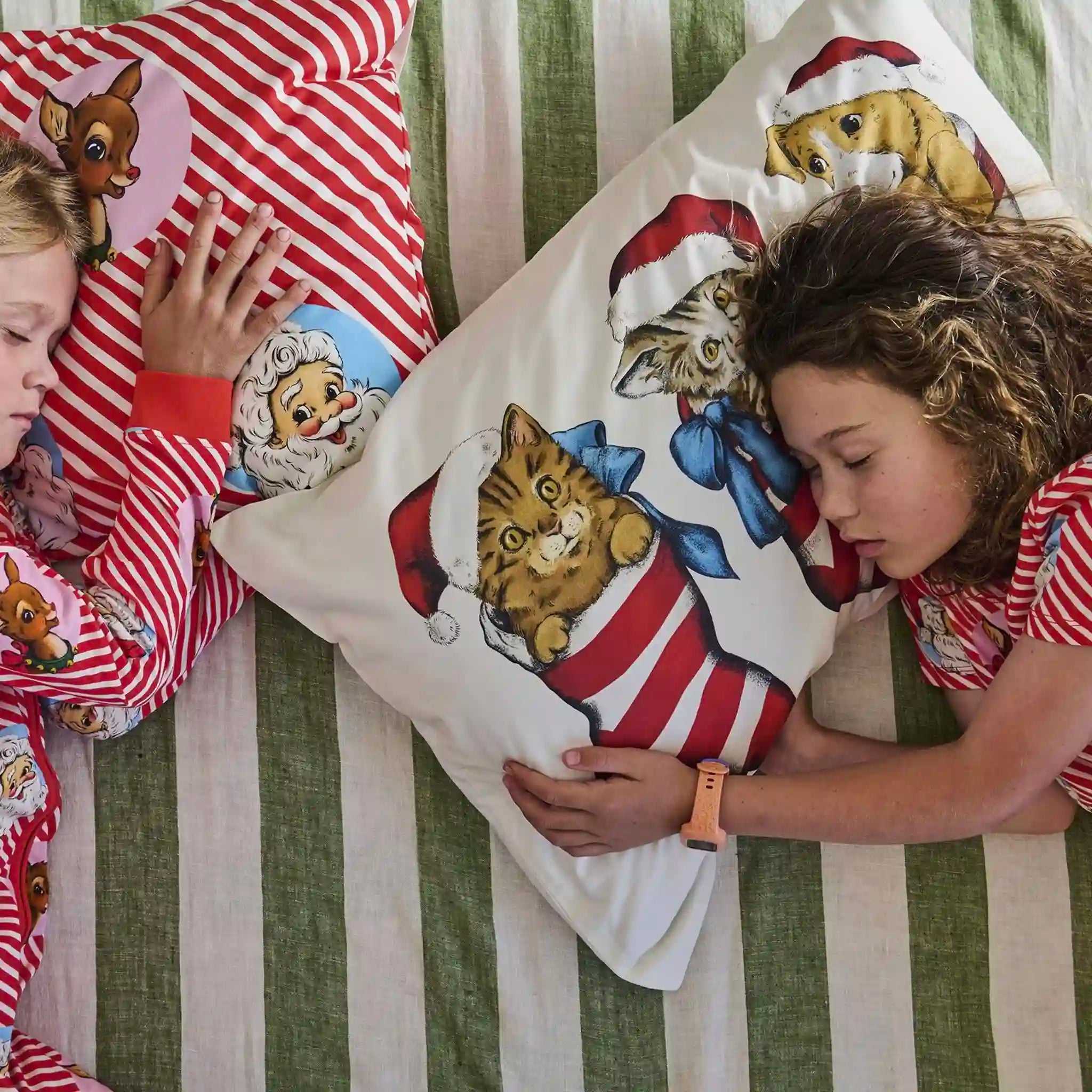 Children in pajamas with Christmas-themed pillows featuring animals on a striped bed.