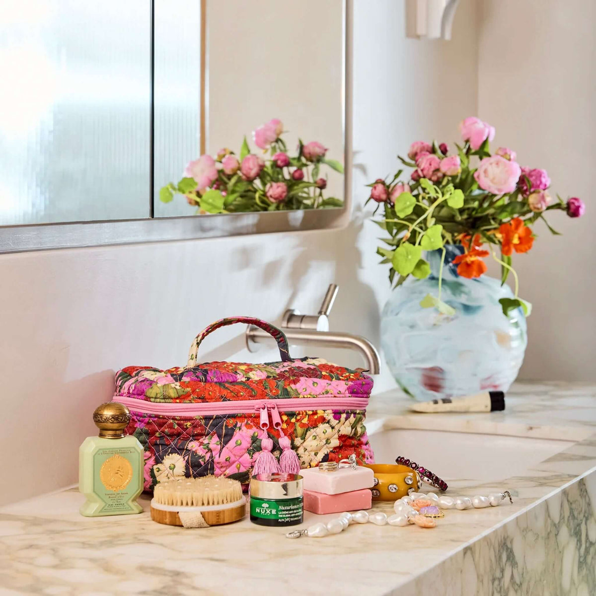 Kip & Co Quilted Toiletry Case - Bush Blossom on a bathroom vanity with beauty products and flowers.