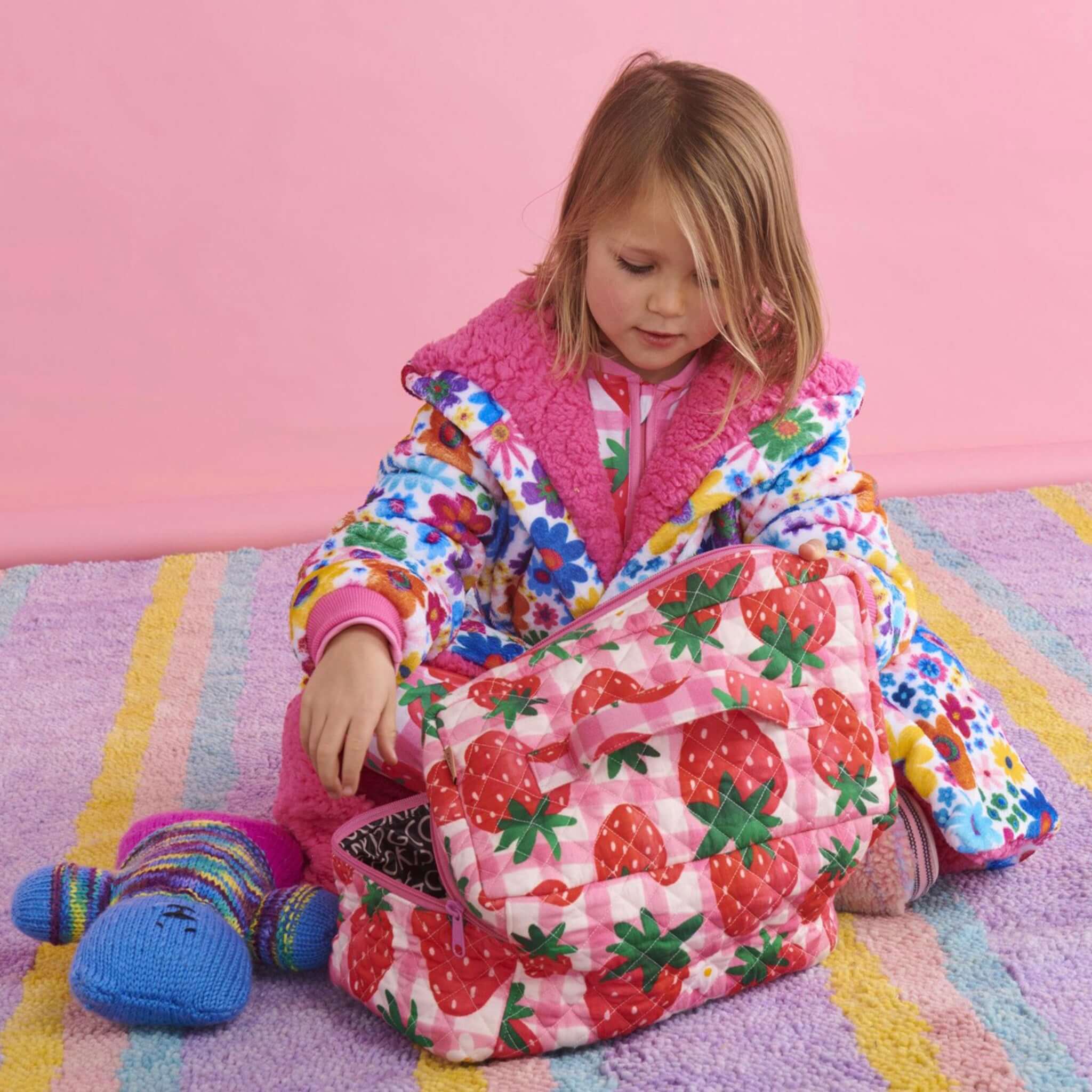 Alt Tag: Kip & Co Quilted Toiletry Case - Strawberry Jam strawberry print quilted cotton zip toiletry bag with child opening on rug