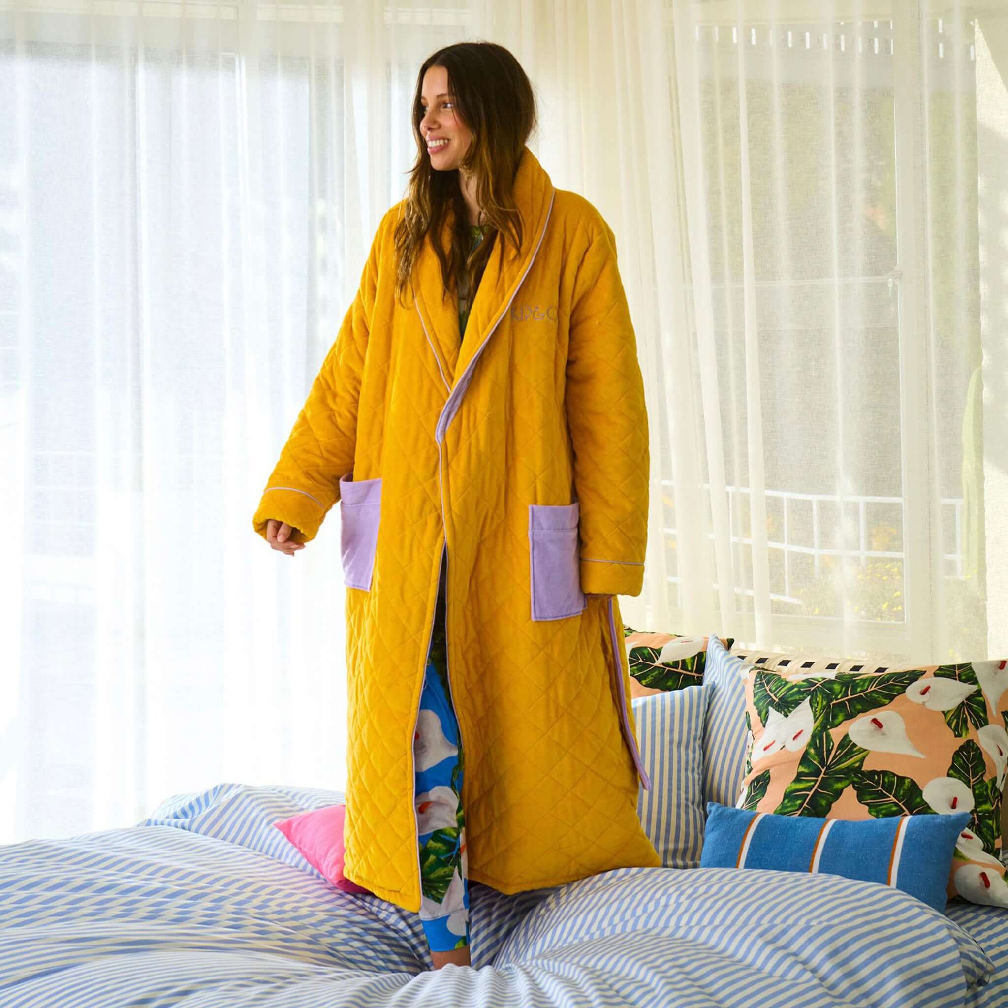 Alt Tag: Kip & Co Quilted Velvet Robe - Lavender Honey quilted velvet robe in honey yellow with mauve pockets and tie, worn indoors