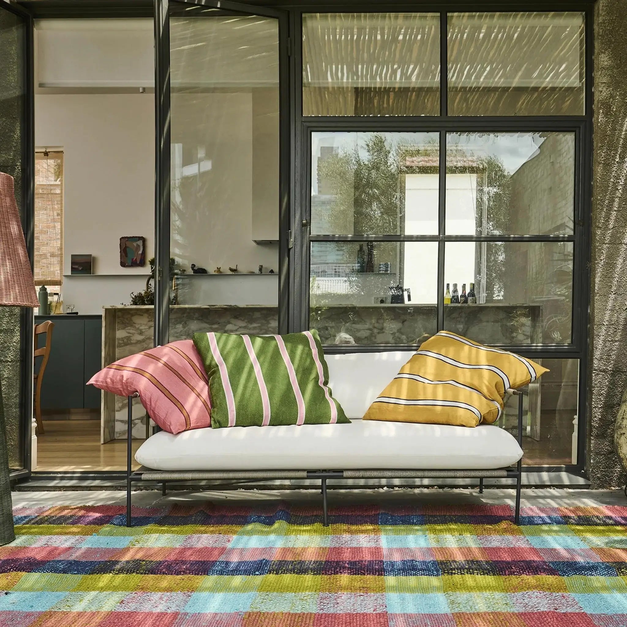Modern outdoor sofa with colorful cushions on a patio with a glass door in the background.