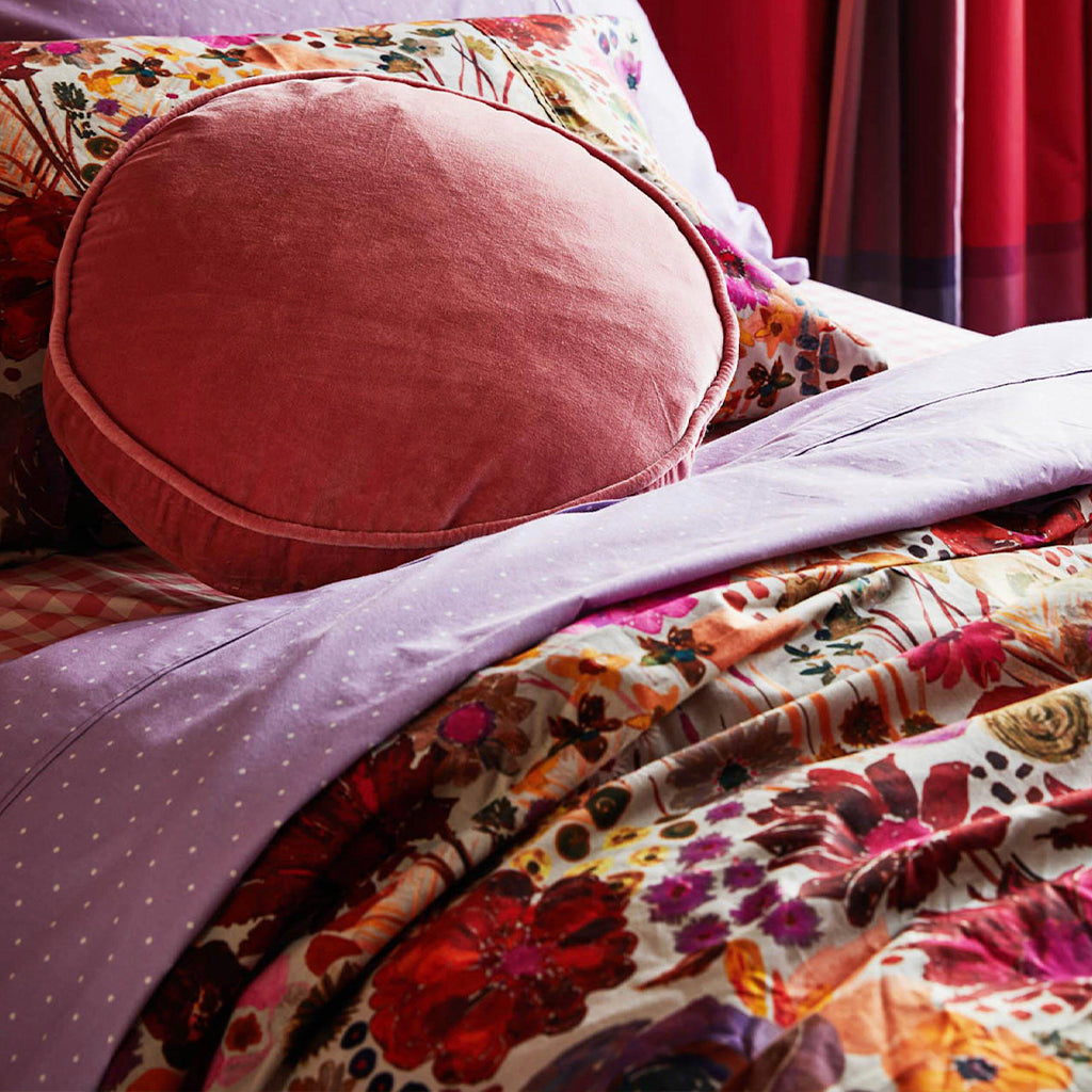 Round pink cushion on a bed.