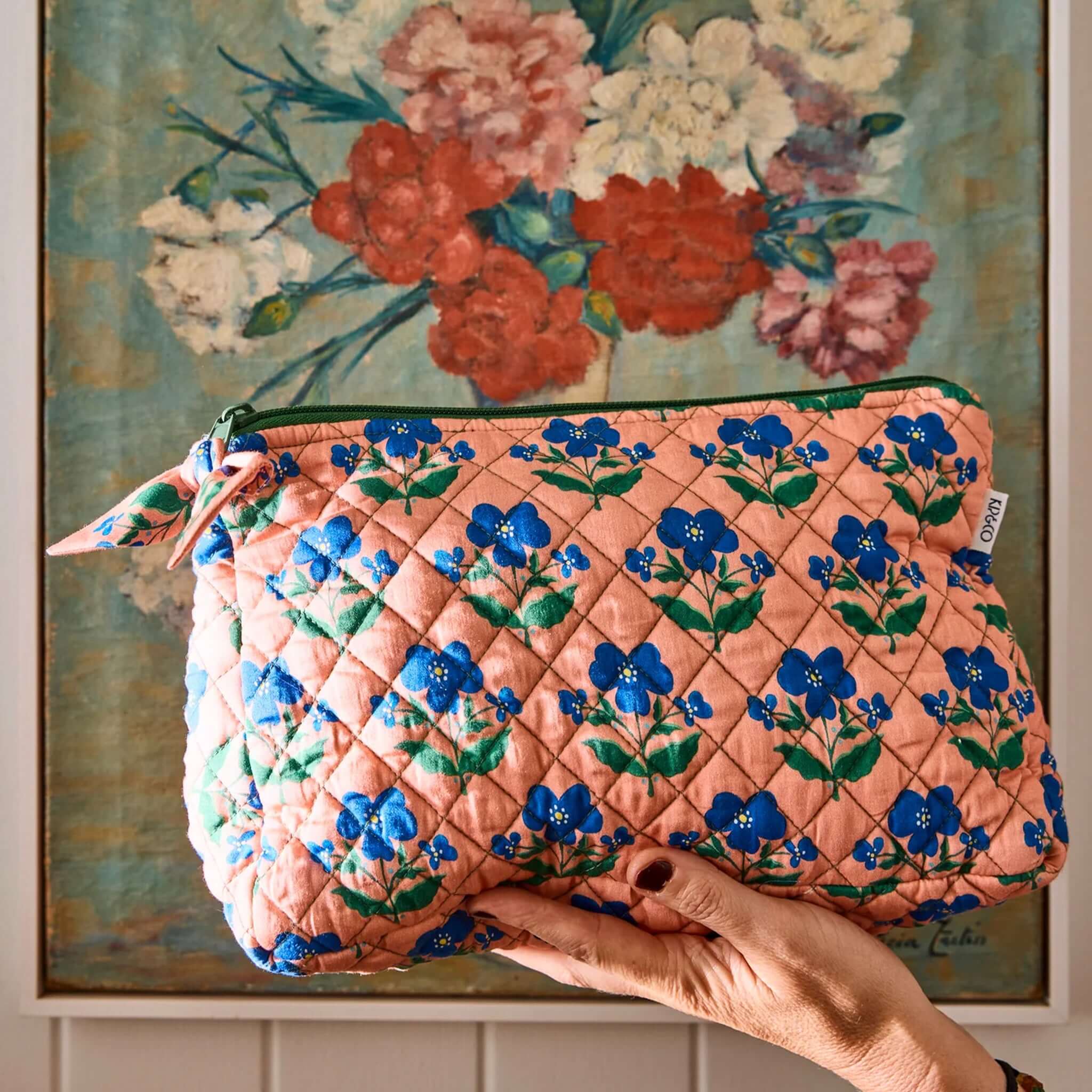 Kip & Co x Anna Spiro Quilted Toiletry Purse - Indian Summer Rose held against floral artwork background.
