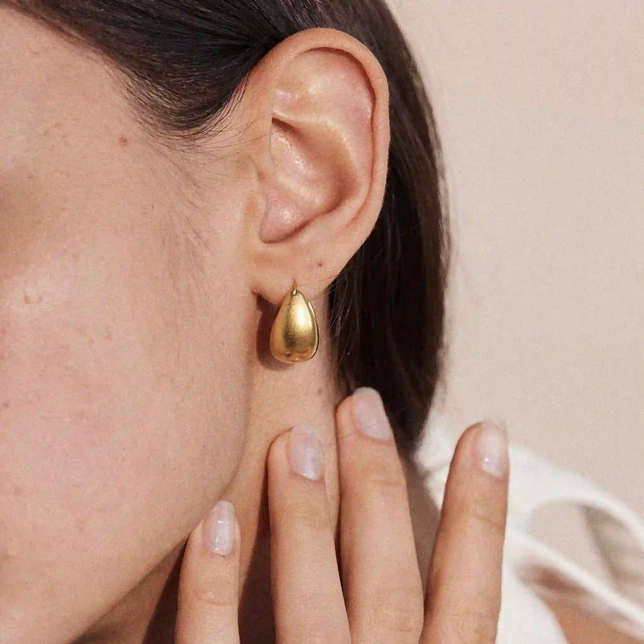 Gold teardrop earring worn by a person with a neutral background