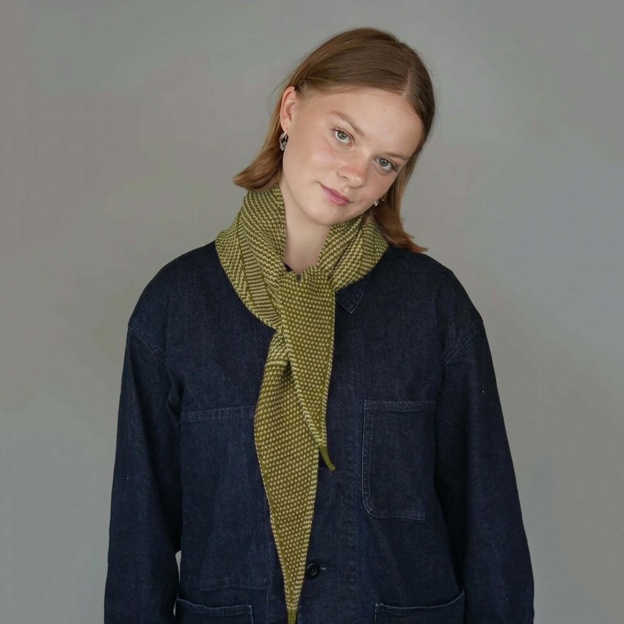 Knit Shepherd Taranaki Merino Neckerchief - Pikopiko Green worn by a model against a grey background.