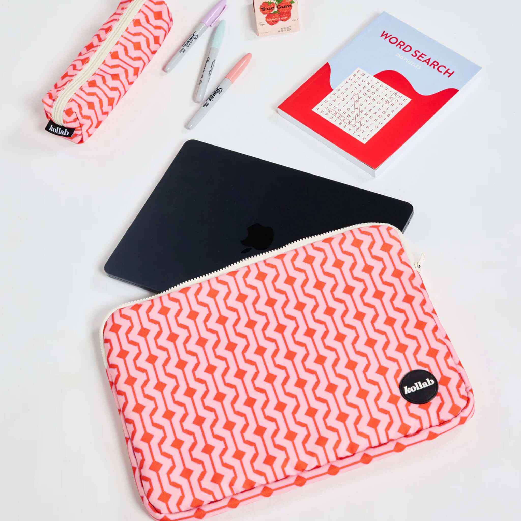 Pink and white patterned pouch with a black item inside, surrounded by stationery items on a light surface.