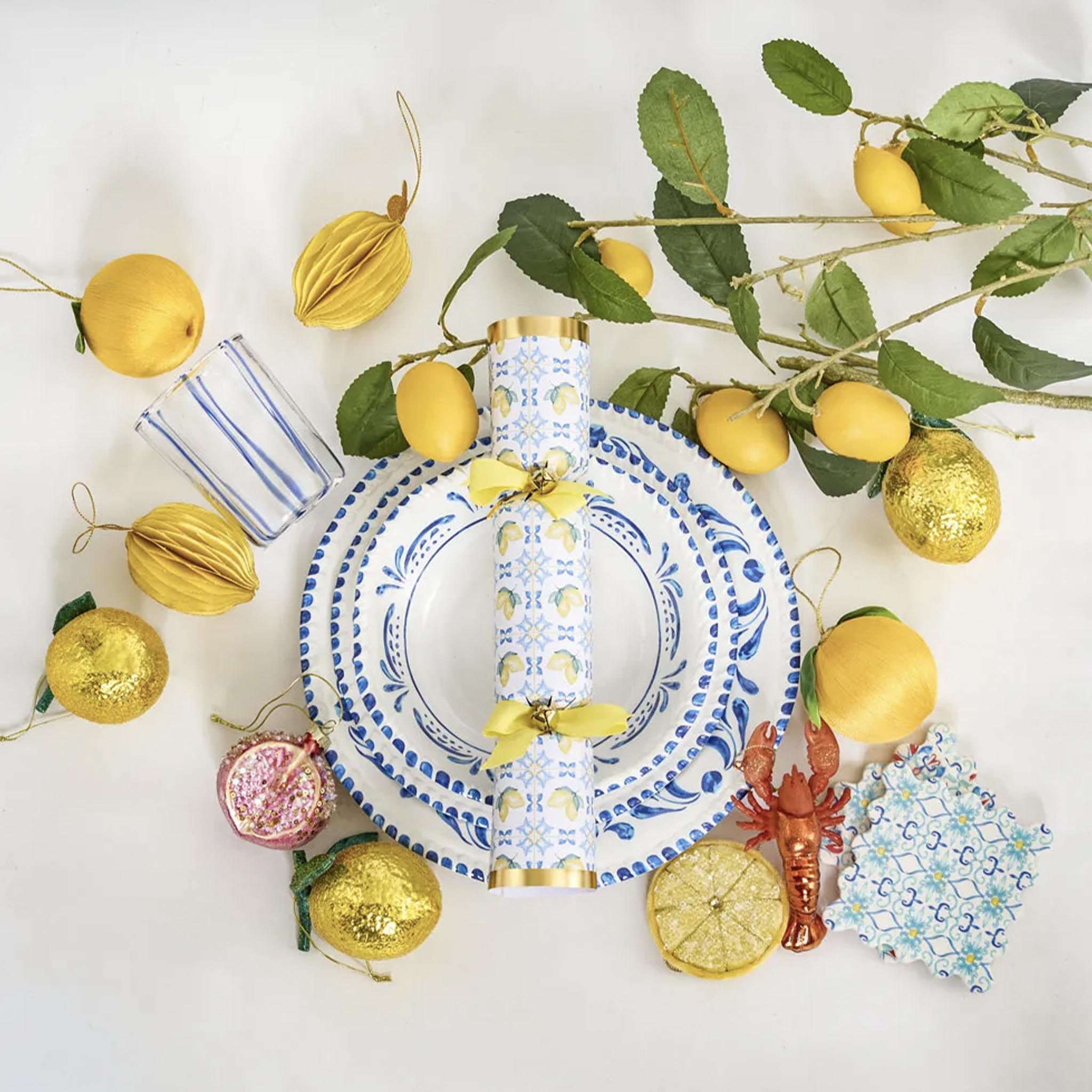 Decorative table setting with lemons, gold balls, and a lobster ornament on a white background.
