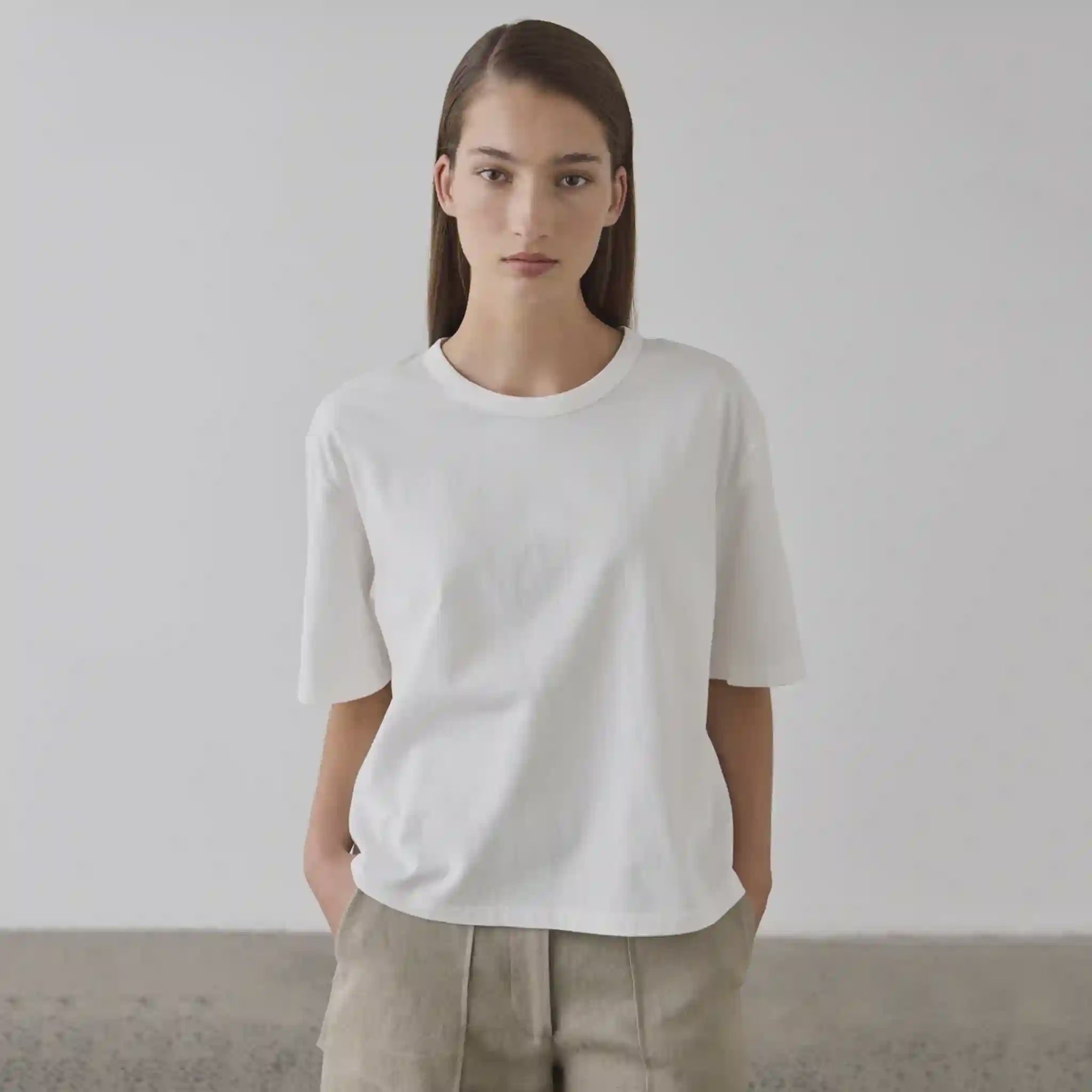 Person wearing a plain white t-shirt and beige pants against a neutral background