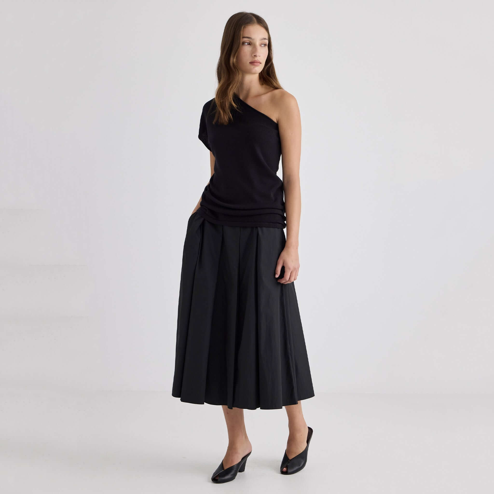 Model wearing Laing Ellis Pleated Skirt - Black with a black top and stylish mules.