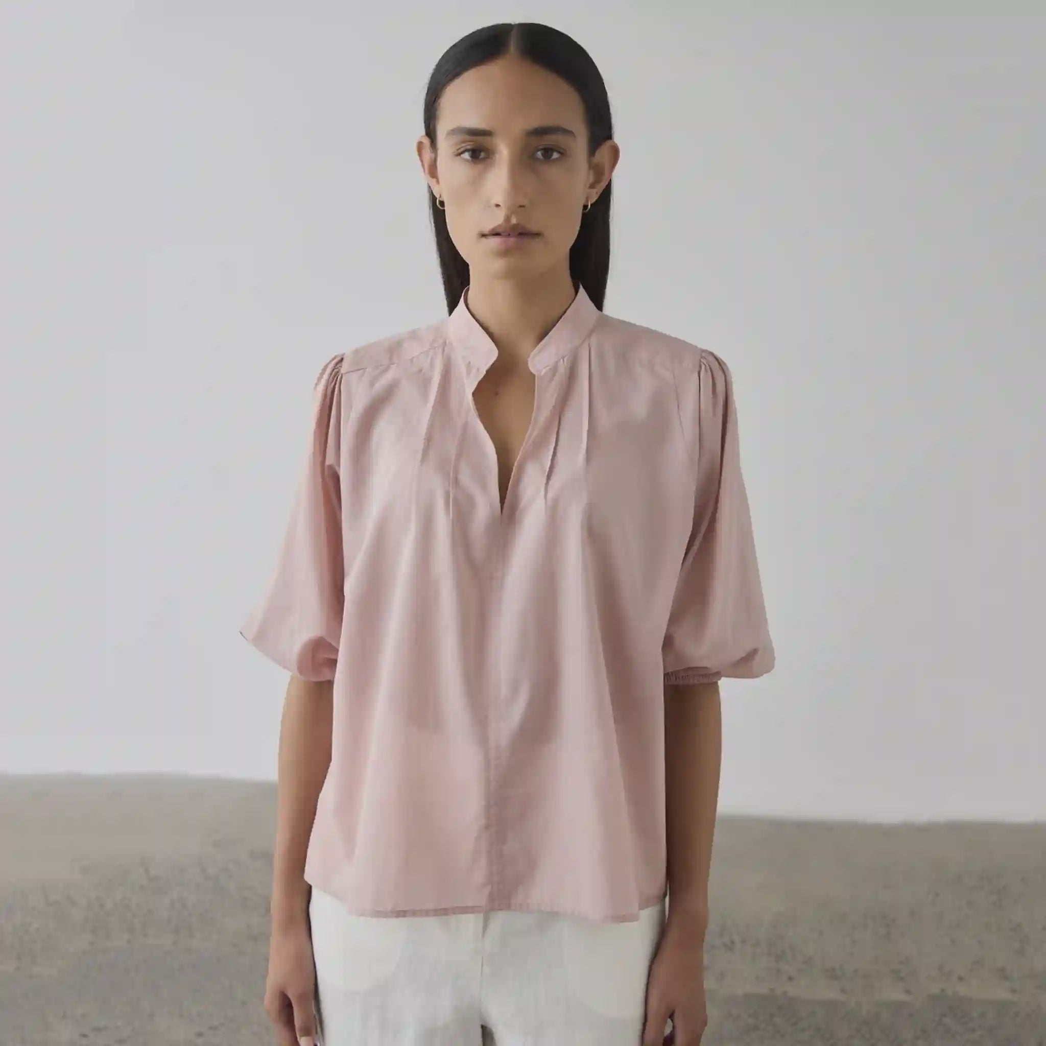Person wearing a light pink blouse against a plain background
