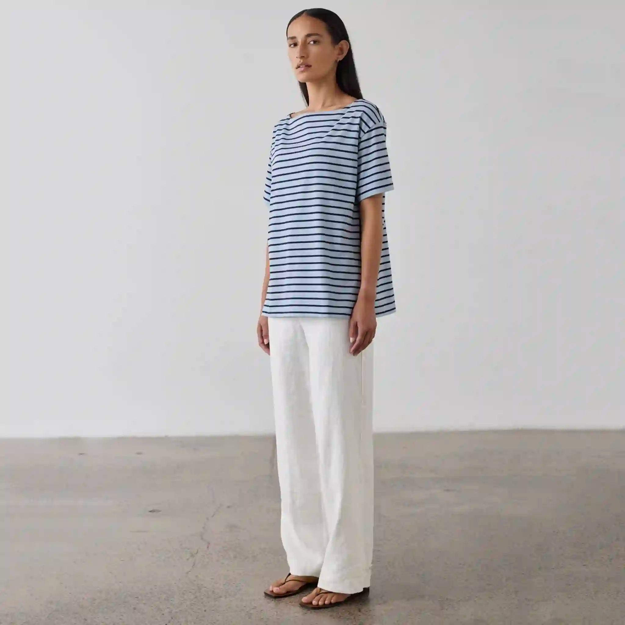 Woman wearing a blue and white striped shirt and white pants against a plain background