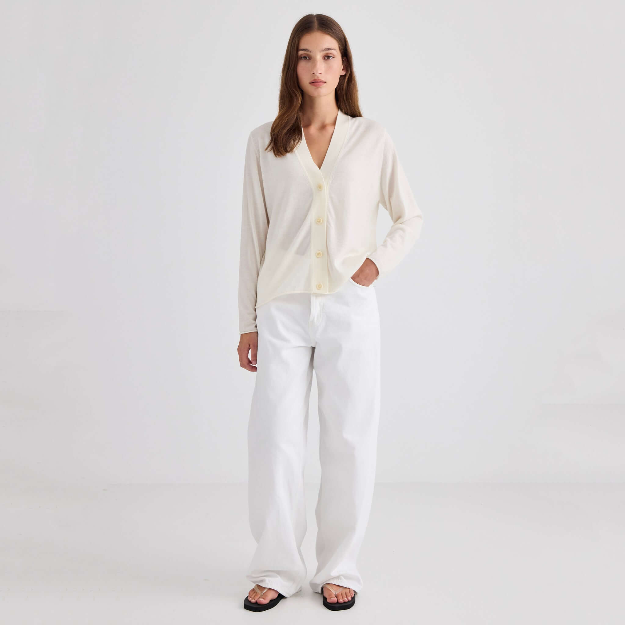 Laing Liv V-Neck Merino Cardigan - Cream worn by a model with white pants in a minimalist setting.