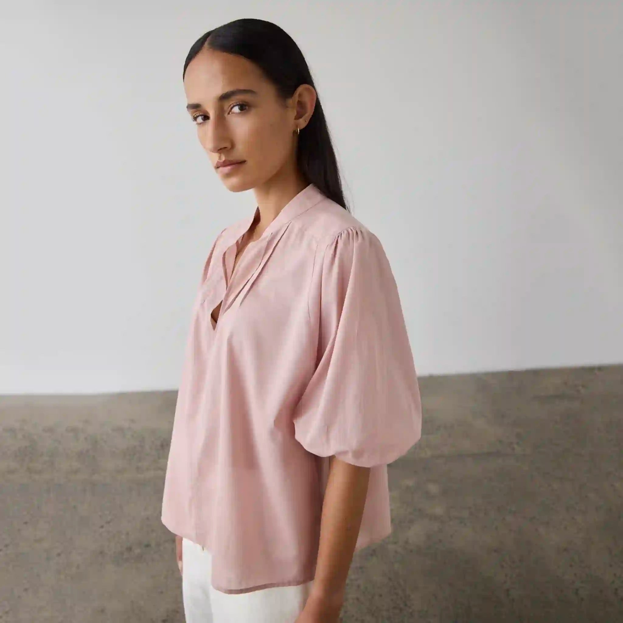 Woman wearing a light pink blouse with puffed sleeves against a neutral background