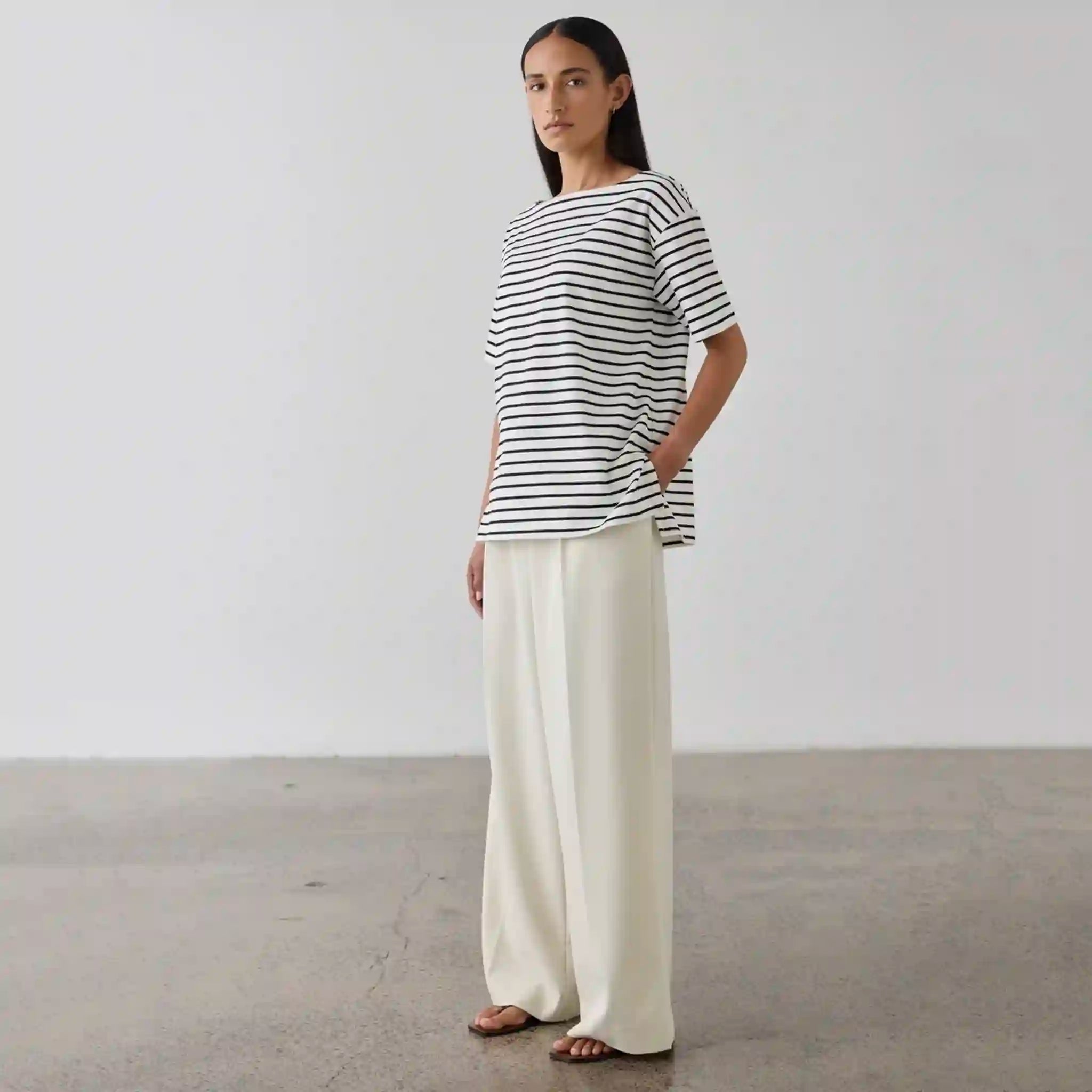 Woman wearing a black and white striped shirt and white pants against a plain background