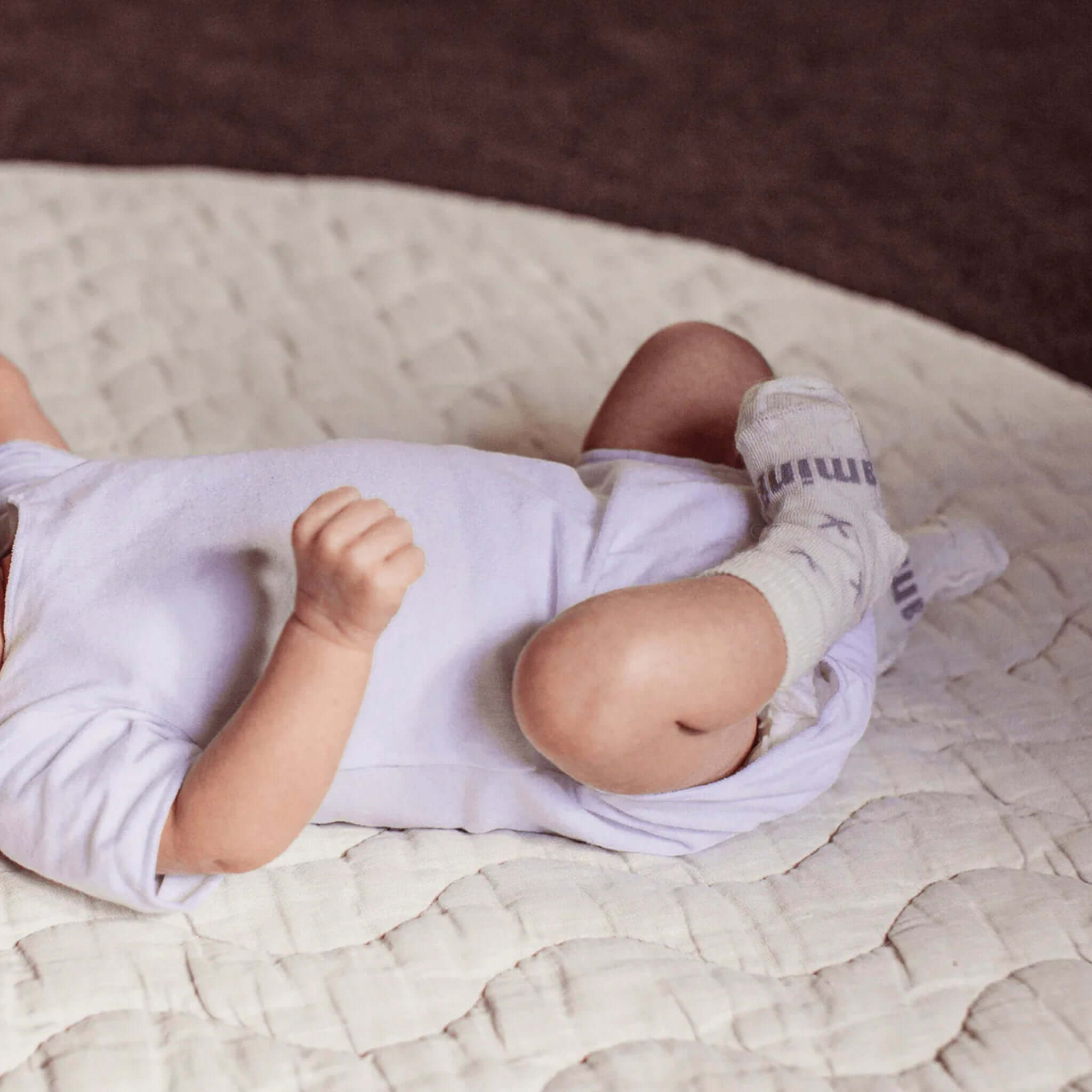 Baby wearing Lamington Merino Crew Baby Socks - Fox, lying on a soft quilted surface.