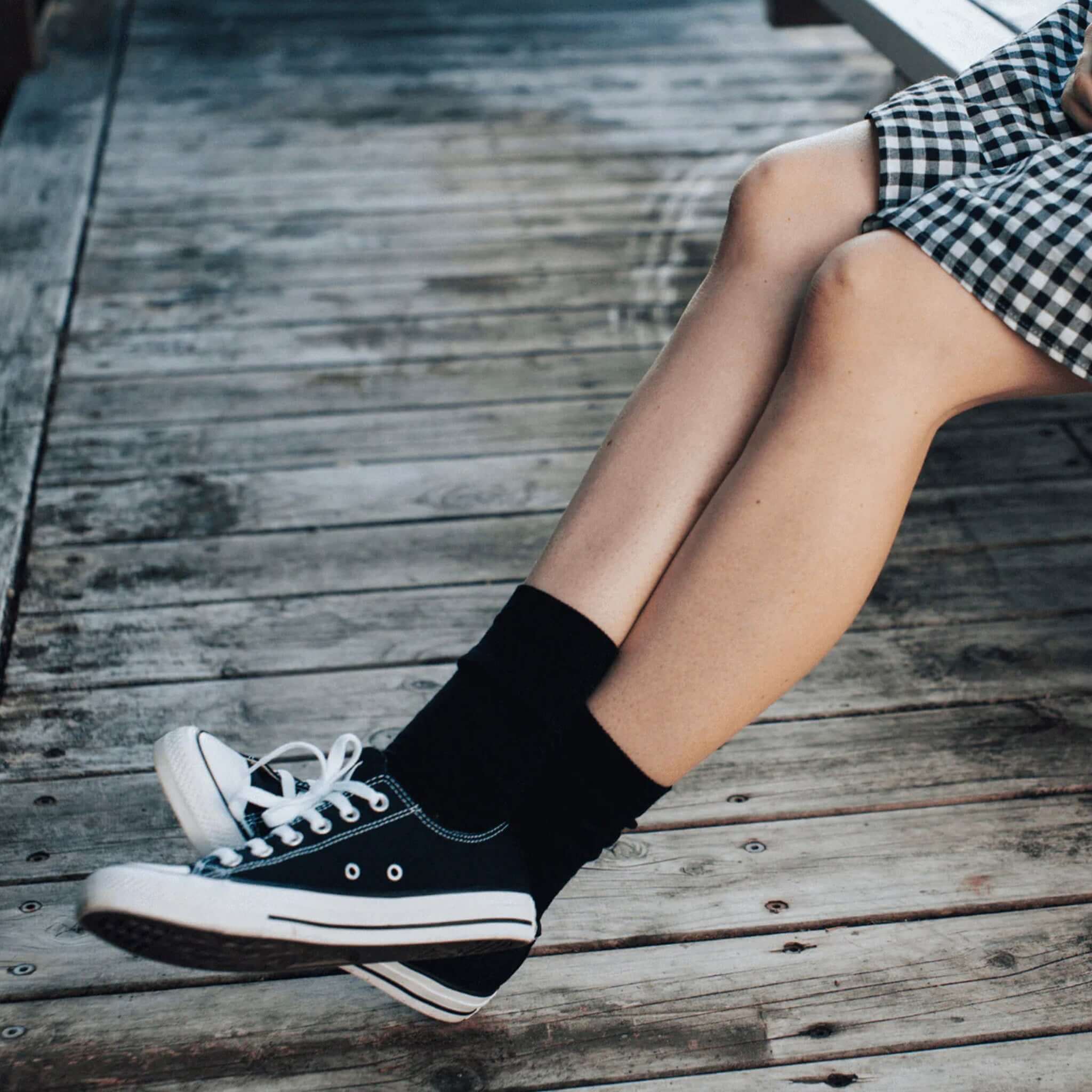 Lamington Merino Adult Crew Socks - Black worn with black sneakers on a wooden deck.