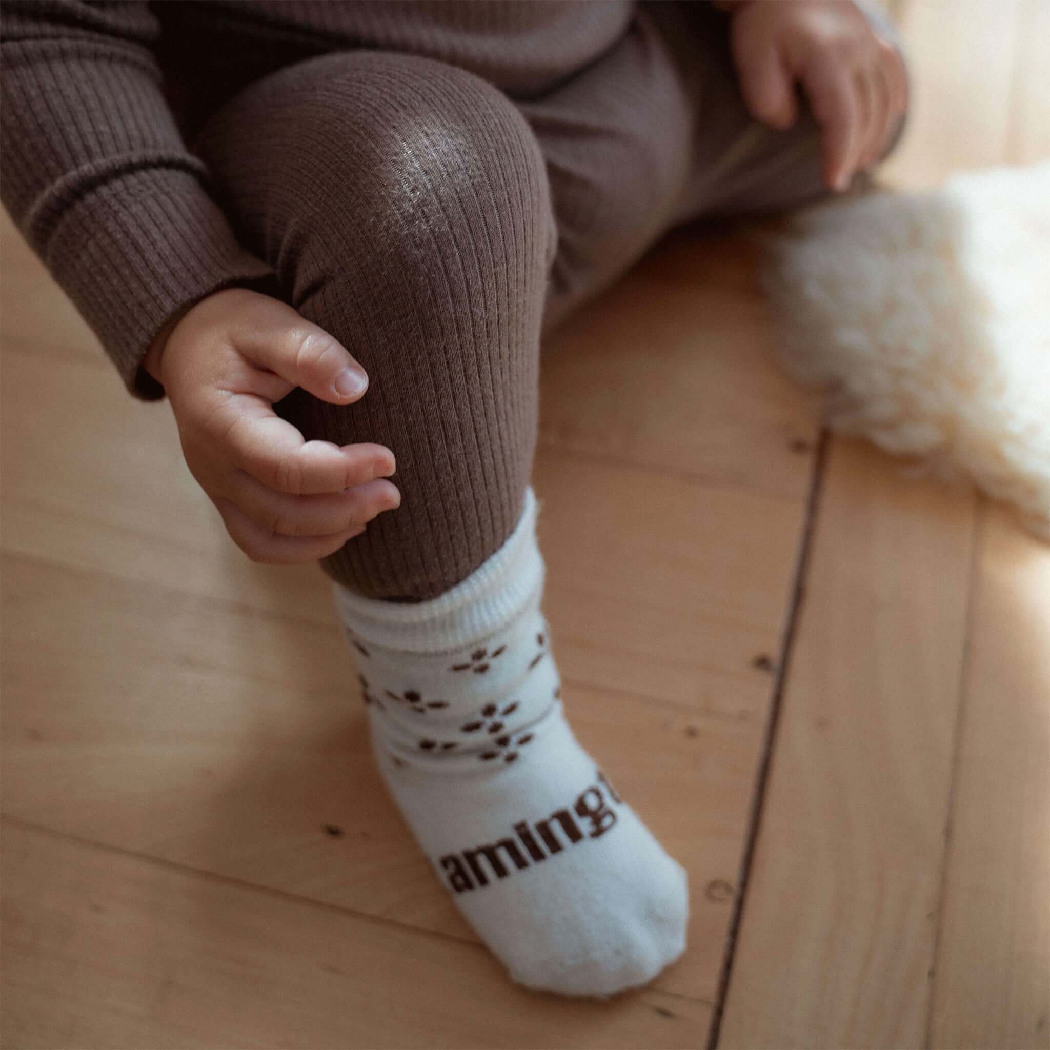 Baby wearing Lamington Merino Crew Baby Socks - Autumn with brown four-petal flowers on a cream background.