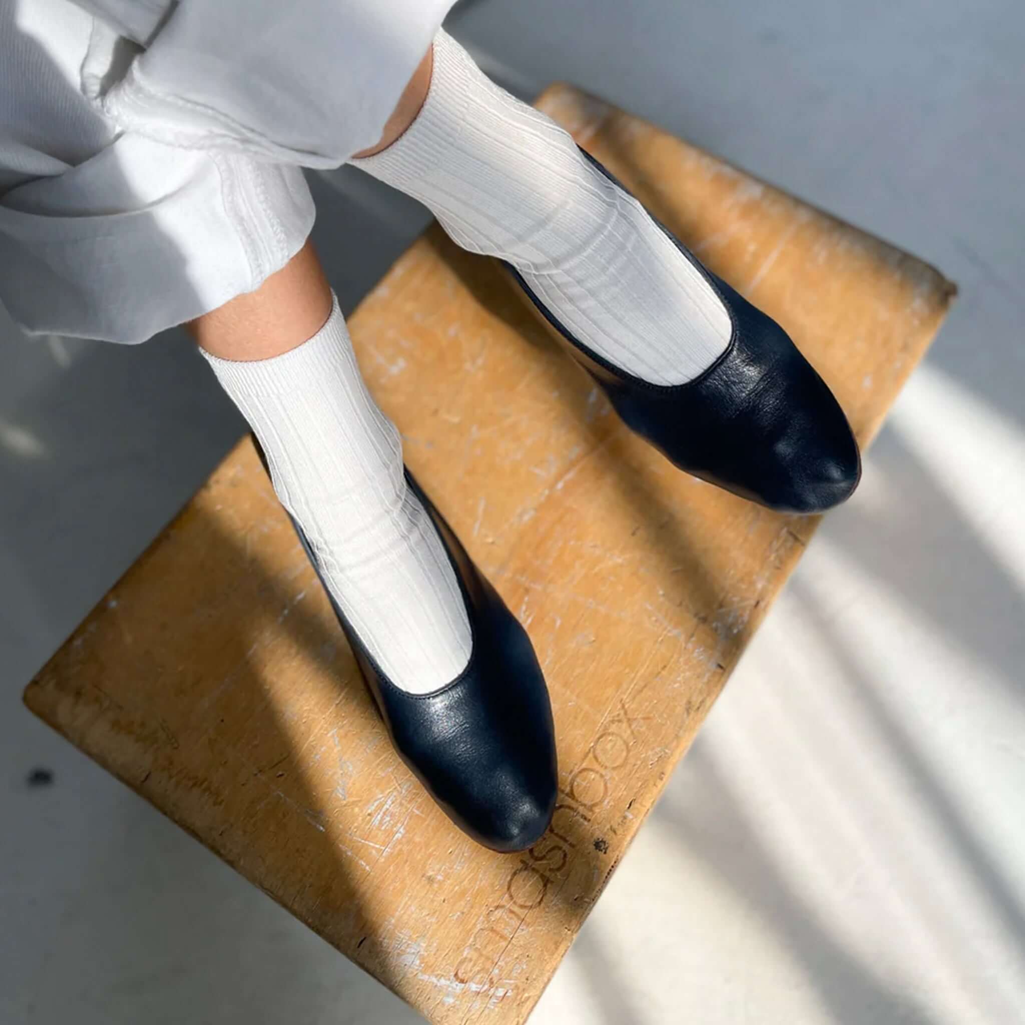 Le Bon Shoppe Her Cotton Socks - Classic White paired with black shoes on a wooden stool.