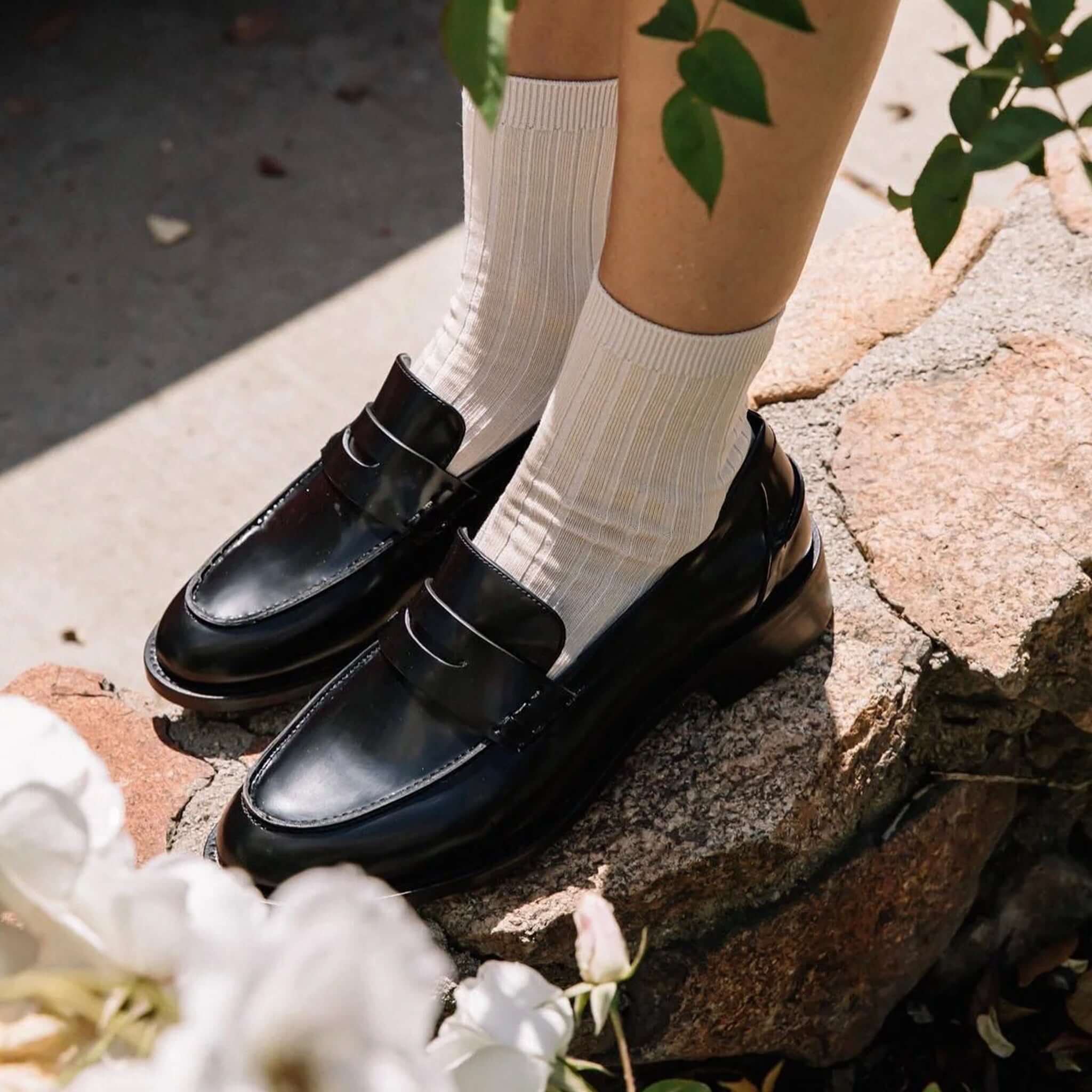 Le Bon Shoppe Her Cotton Socks - Porcelain styled with classic black loafers on a stone pathway surrounded by greenery.